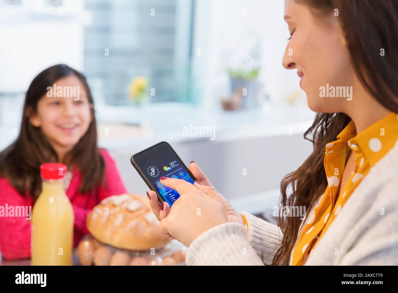 Tochter beobachtet Mutter mit Smartphone in der Küche Stockfoto