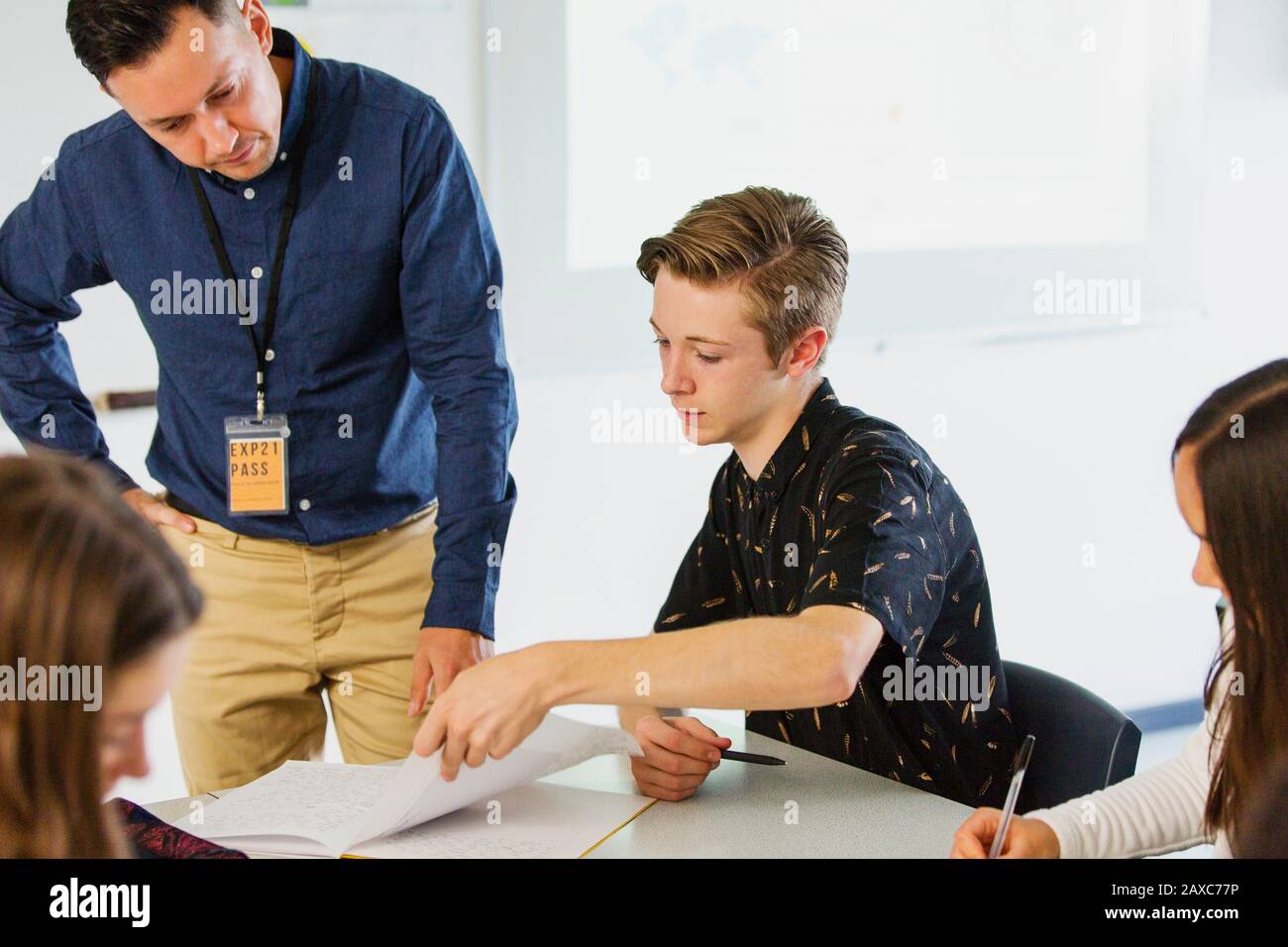 Männliche High-School-Lehrerin hilft Jungschülern bei Hausaufgaben im Klassenzimmer Stockfoto