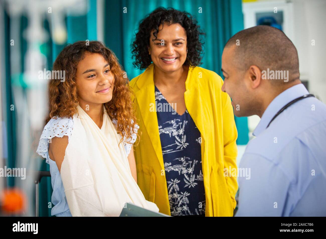 Männliche Kinderärztin spricht mit Mädchen Patient mit Arm in Schlinge im Untersuchungsraum Stockfoto