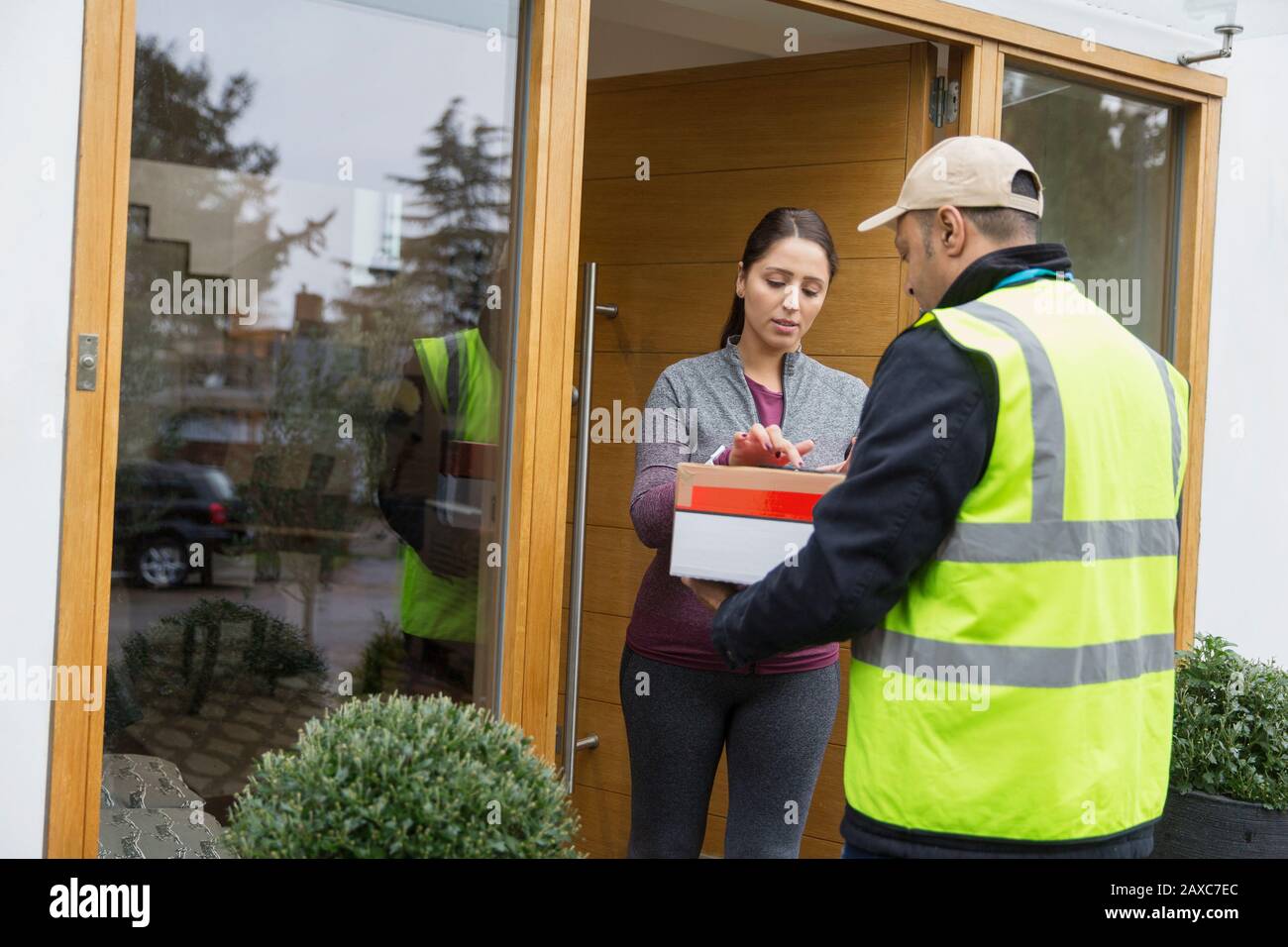 Frau, die sich für ein Paket von einem Zusteller vor der Tür unterschreibt Stockfoto