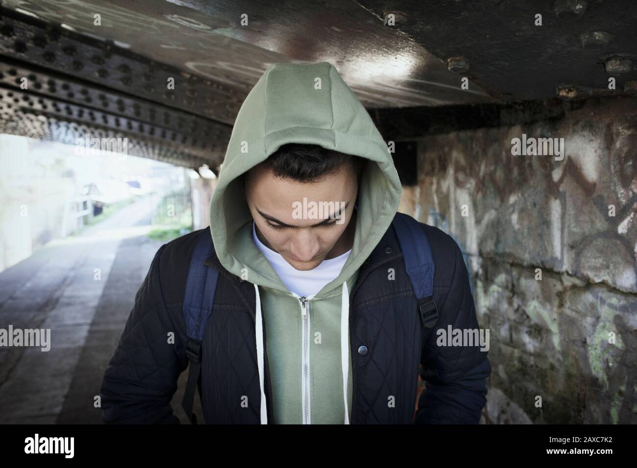 Junger Mann im Hoody, der unter der städtischen Brücke spazieren geht Stockfoto