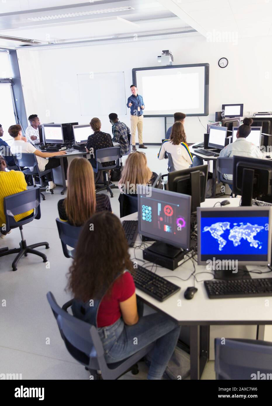 Schüler mit hohen Schülern an Computern, die Lehrer auf der Projektionsleinwand im Klassenzimmer anhören Stockfoto