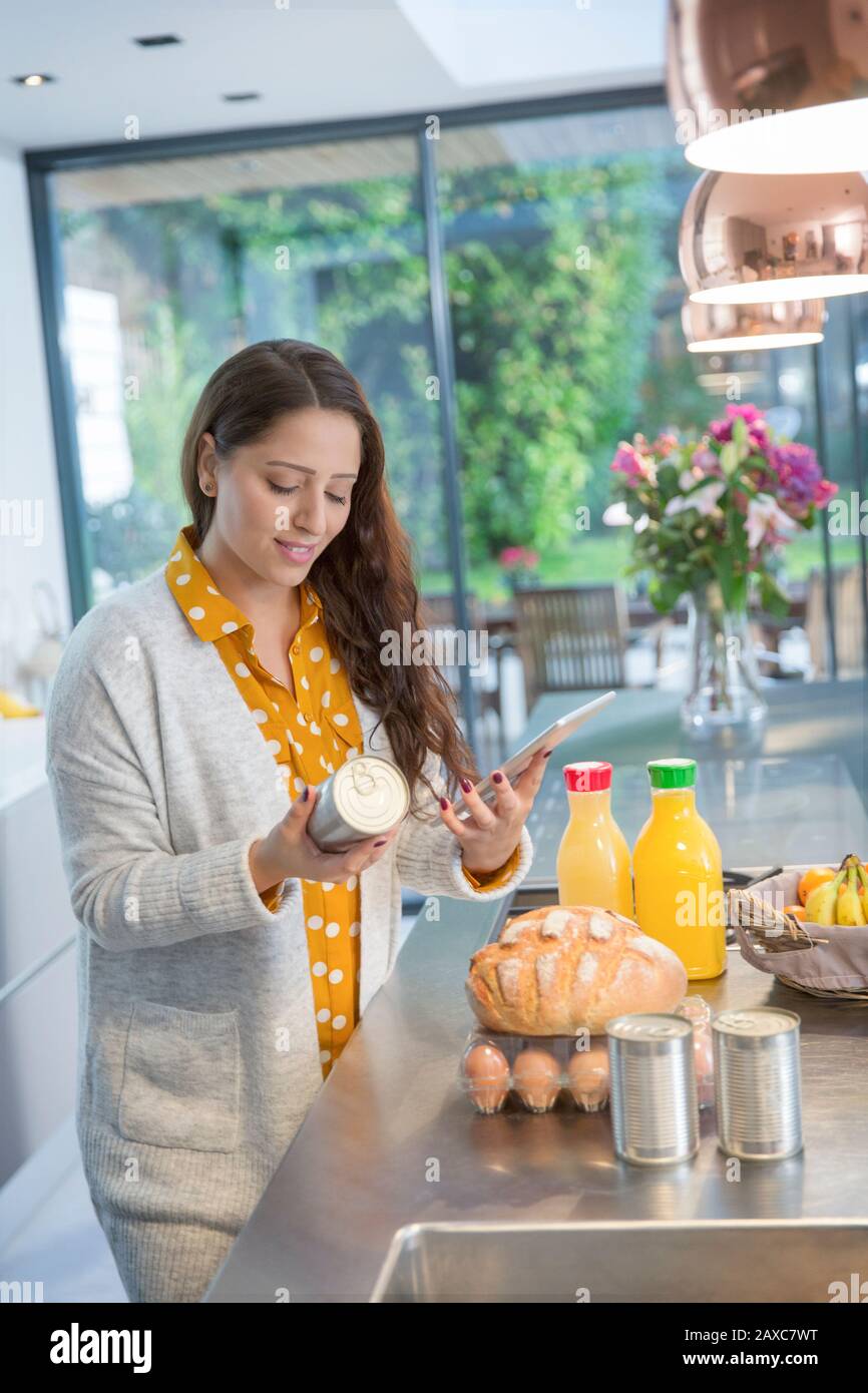 Frau mit digitaler Tablette, die Lebensmitteletiketten in der Küche überprüft Stockfoto