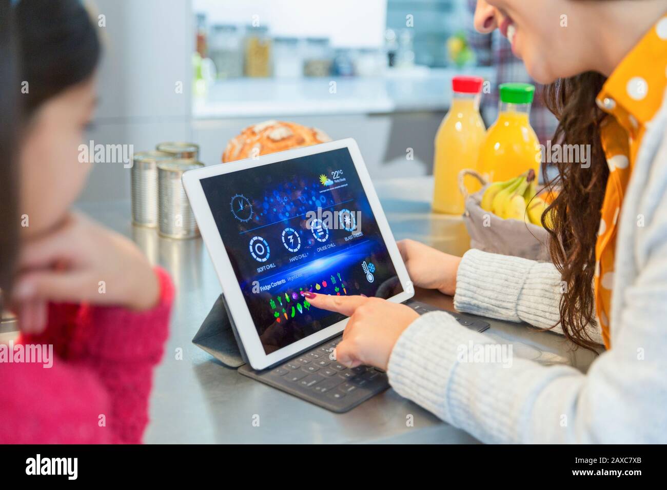 Tochter, die Mutter beobachtet, wie sie Lebensmittellisten auf einem digitalen Tablett in der Küche vorbereitet Stockfoto