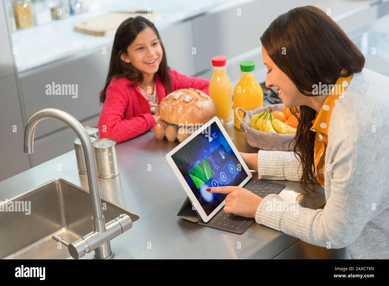 Tochter beobachtet Mutter mit digitalem Tablett in der Küche Stockfoto