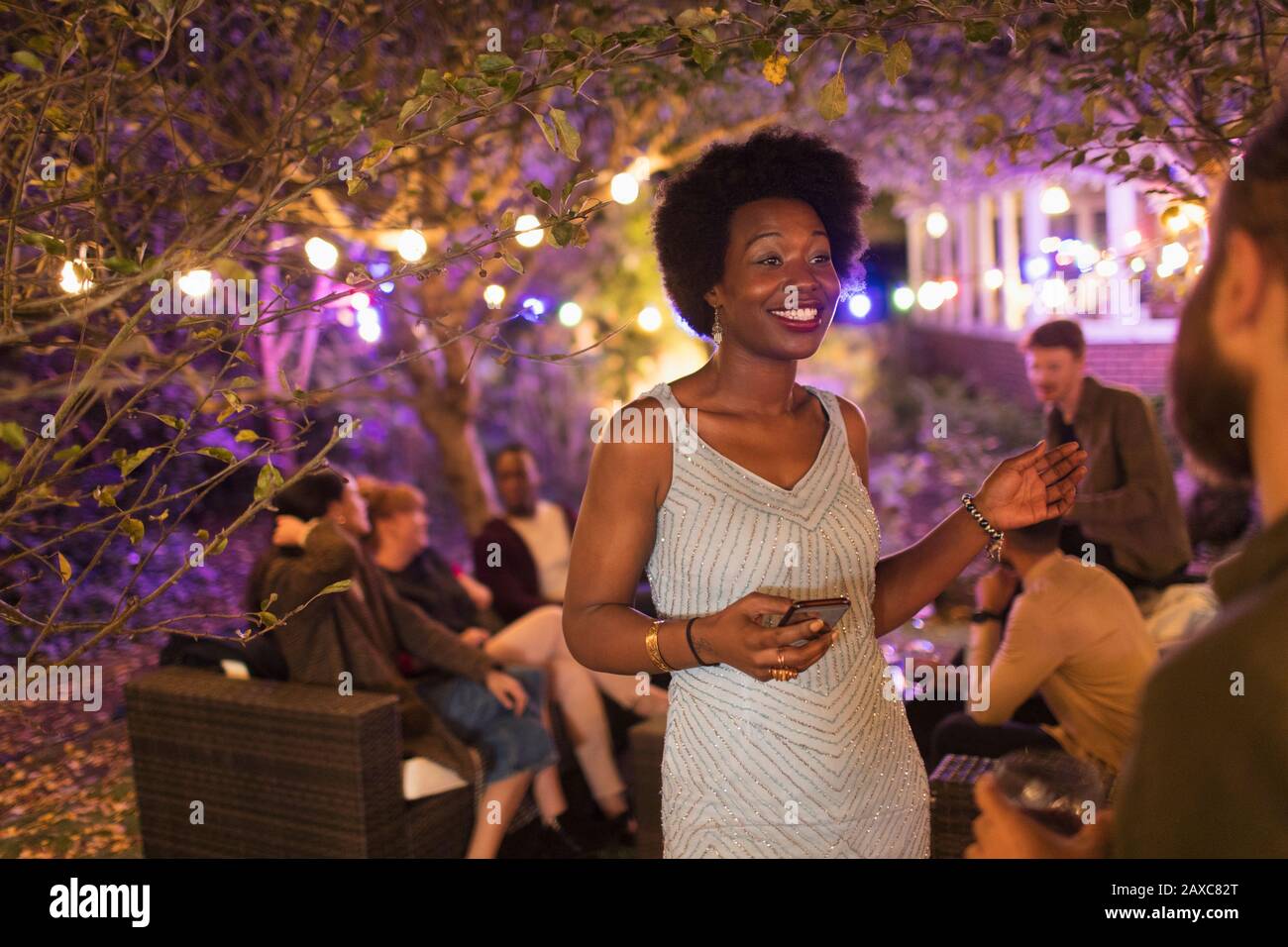 Lächelnde Frau mit Smartphone, die auf der Gartenparty mit einem Freund spricht Stockfoto