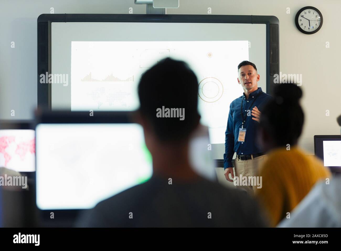 Junger männlicher Lehrer, der die Lektion auf der Projektionsleinwand im Klassenzimmer führt Stockfoto