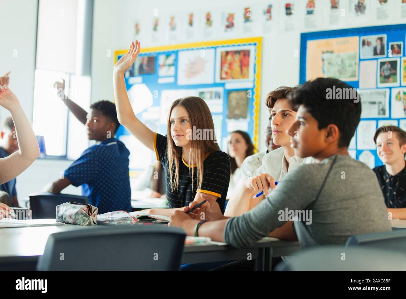 Schüler der High School mit erhobenen Händen, die während des Unterrichts im Klassenzimmer Fragen stellen Stockfoto