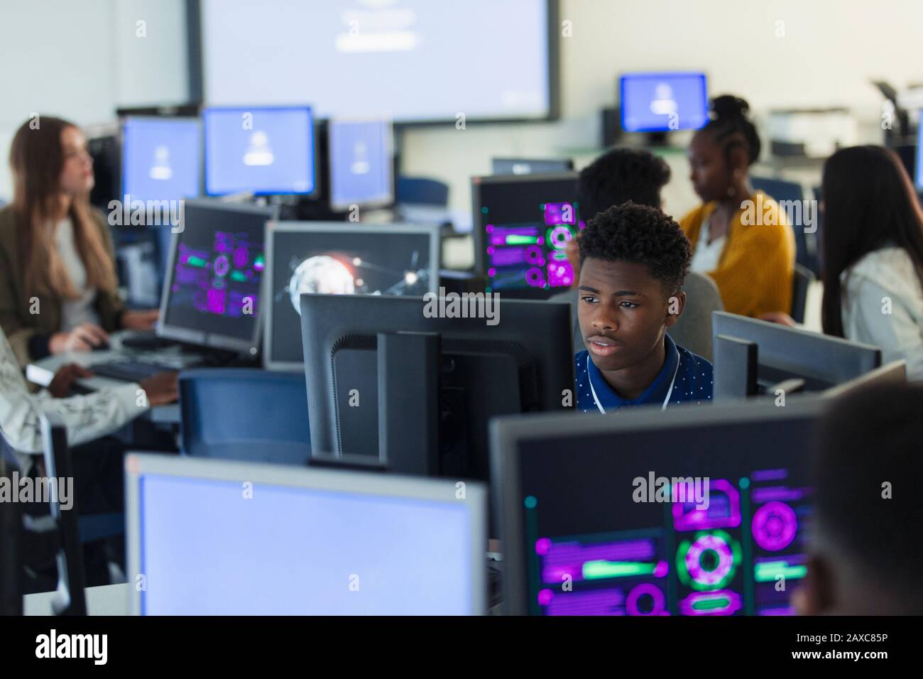 Schüler mit hohem Jungen, die im dunklen Computerlabor Computer verwenden, mit Schwerpunkt Stockfoto