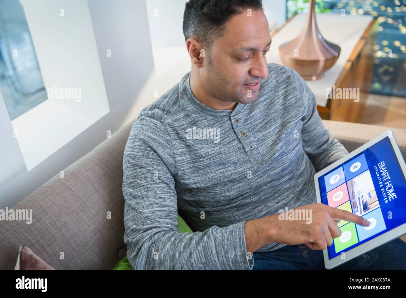 Mann setzt Smart Home Alarm vom digitalen Tablet auf dem Wohnzimmer Sofa Stockfoto