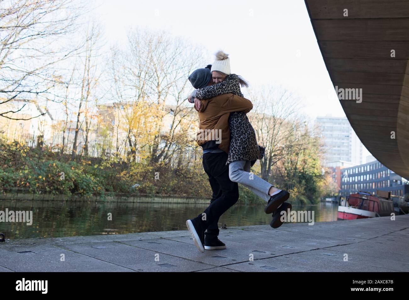 Fröhliches junges Paar, das sich entlang des städtischen Kanals umarmt Stockfoto