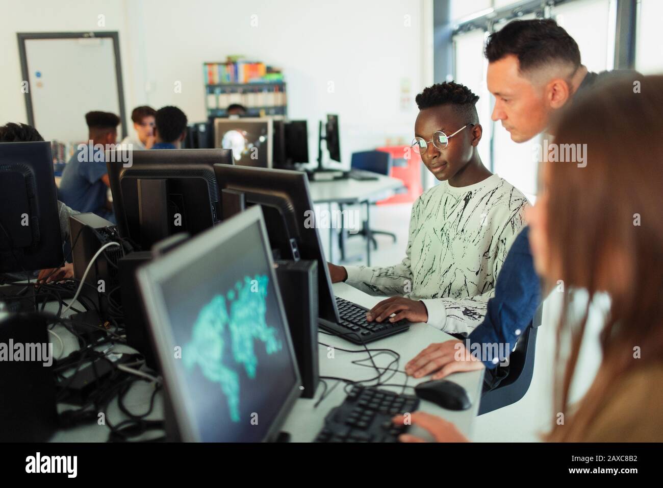 Junger junger Lehrer, der jungen Studenten hilft, Computer im Computerlabor zu benutzen Stockfoto