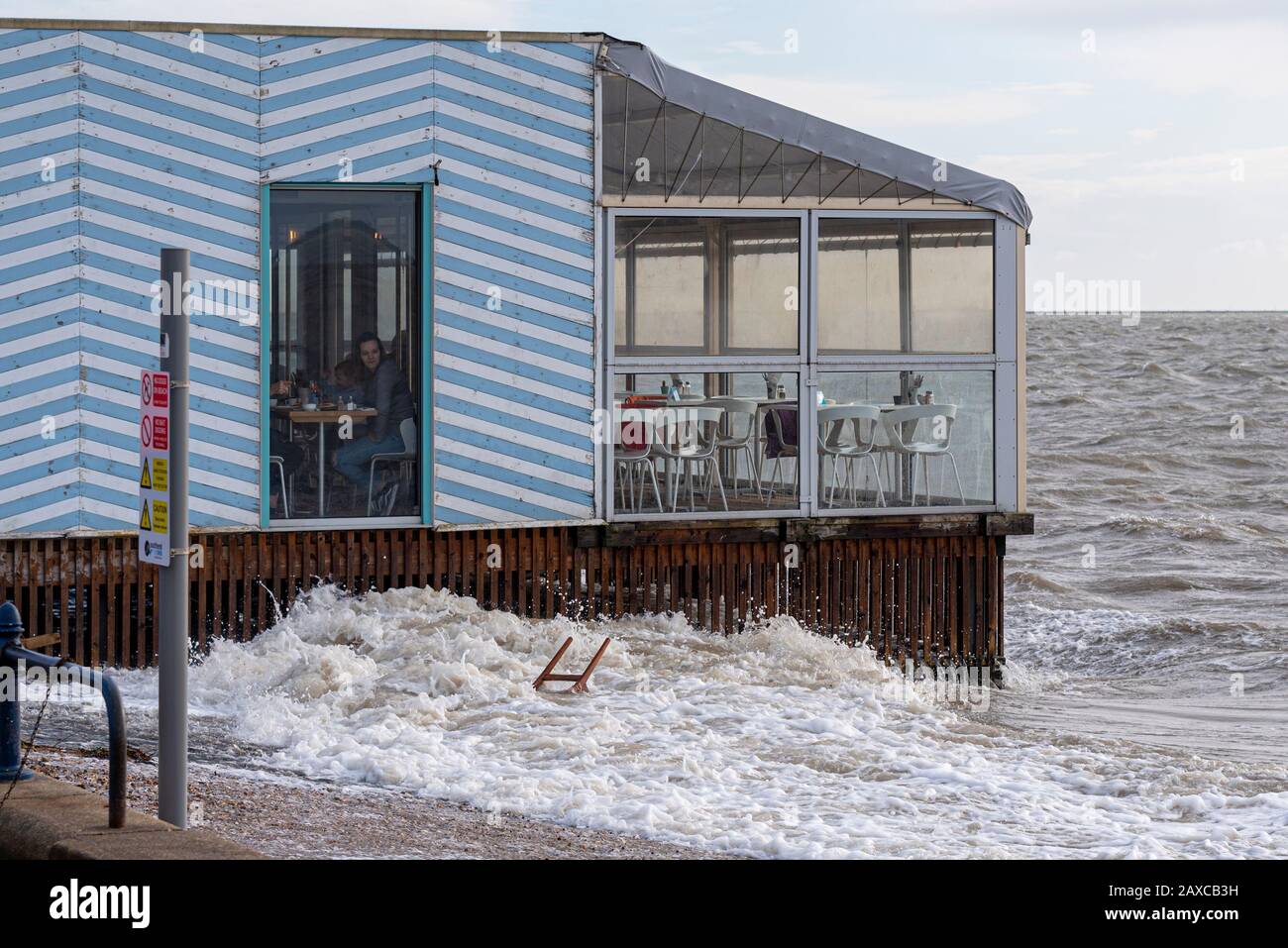 Kunde im Strandrestaurant Beach Hut, der einen Stuhl beobachtet, der von der Sturmflut von Storm Ciara aufgespült wurde. Person im Café auf Stelzen über dem Meer Stockfoto