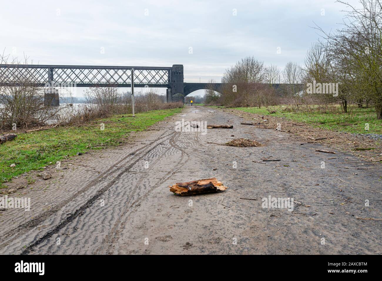Ein Dirt-Bike-Weg am Ufer eines Flusses in Westdeutschland nach einem Hochwasser, sichtbarem Müll, Baumzweigen und Bahnbrücke. Stockfoto