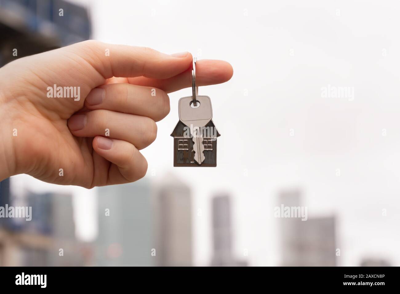 Die Hand, die einen Schlüssel zu einem Traumhaus vor dem Hintergrund der städtischen Skyscapes hält. Das Konzept, ein Haus oder eine Wohnung zu mieten oder zu verkaufen, Hypotheken und RE Stockfoto