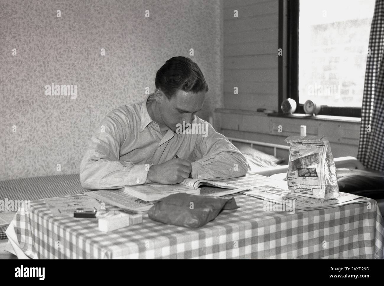 40er Jahre, historisch, Mann in einer Wohnheimat, der an einem mit Vinyl bedeckten Tisch sitzt und etwas in einem Buch studiert, England, Großbritannien. Stockfoto