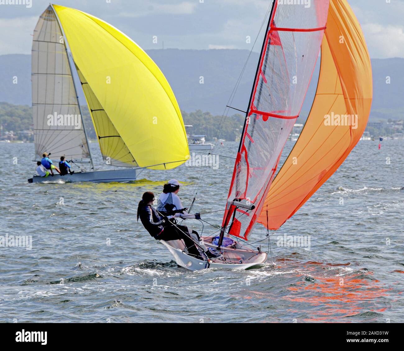 Kinder Segeln kleine Segelboote mit gelben und orangefarbenen Segeln im Wettbewerb. Teamarbeit von jungen Matrosen, die auf dem Salzwasser Lake Macquarie Rennen. Foto für Stockfoto