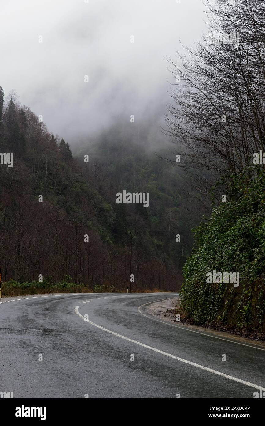 In der Wintersaison eine nasse Straße zwischen den Hügeln biegen. Stockfoto