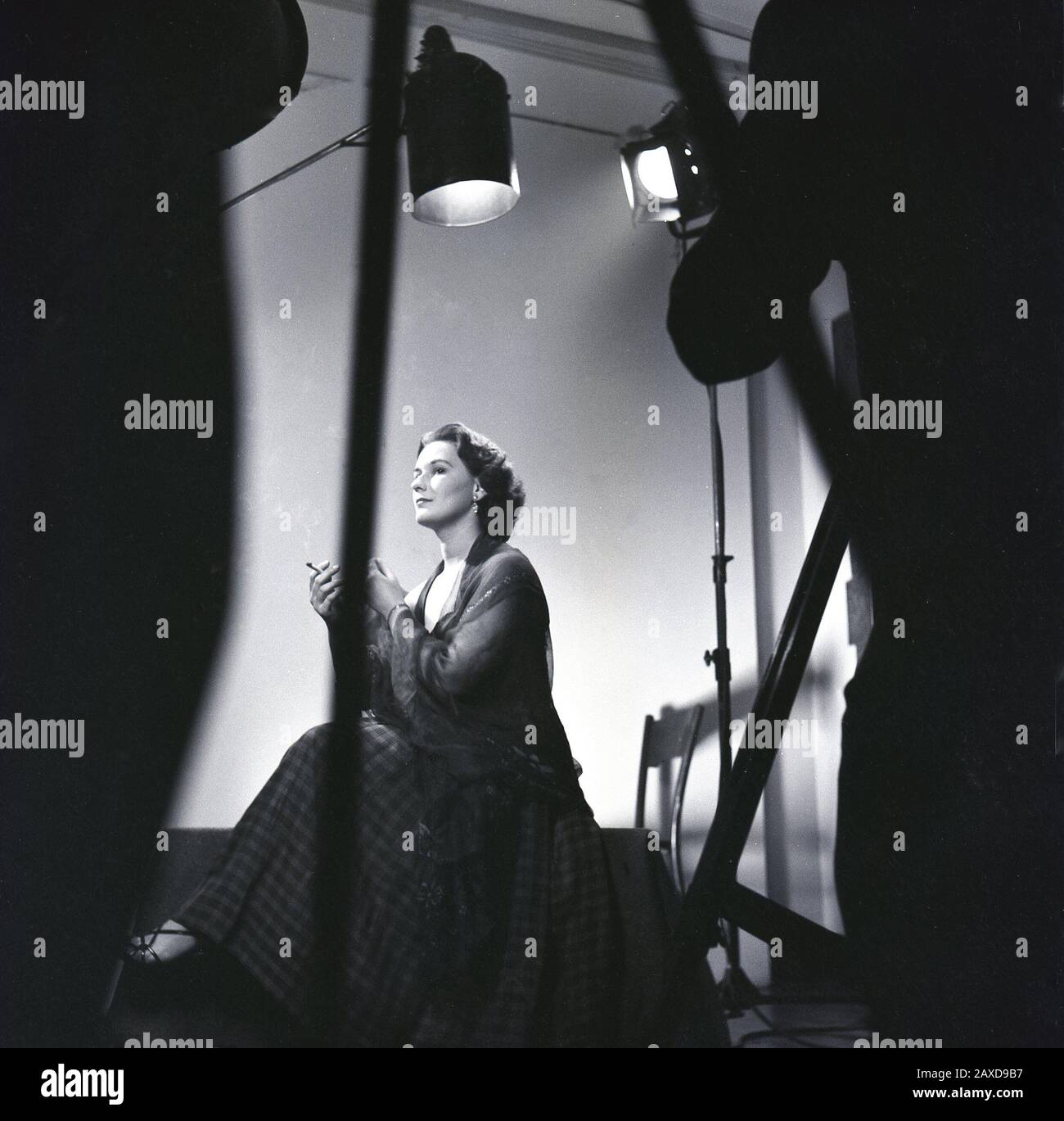 1950er Jahre, historisch, eine Schauspielerin in einem langen Rock, sitzt unter Theaterlichtern, hat eine Pause von den Proben mit einer Zigarette, England, UK. Stockfoto