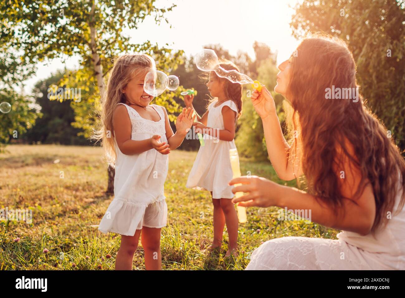 Muttertag. Frau hilft Töchtern, Seifenblasen im Sommerpark zu blasen. Kinder haben Spaß beim Spielen im Freien Stockfoto