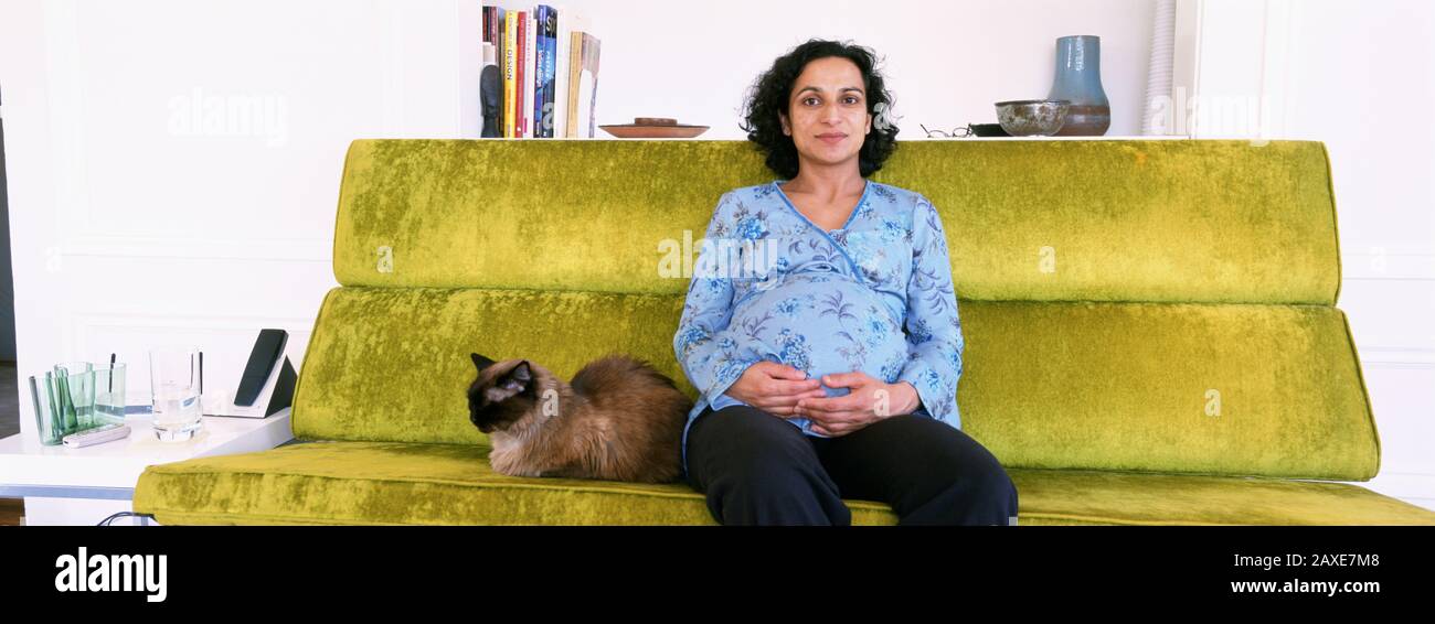 Porträt Einer Schwangeren Frau, Die Mit Ihrer Katze, USA, Auf Einer Couch Sitzt Stockfoto