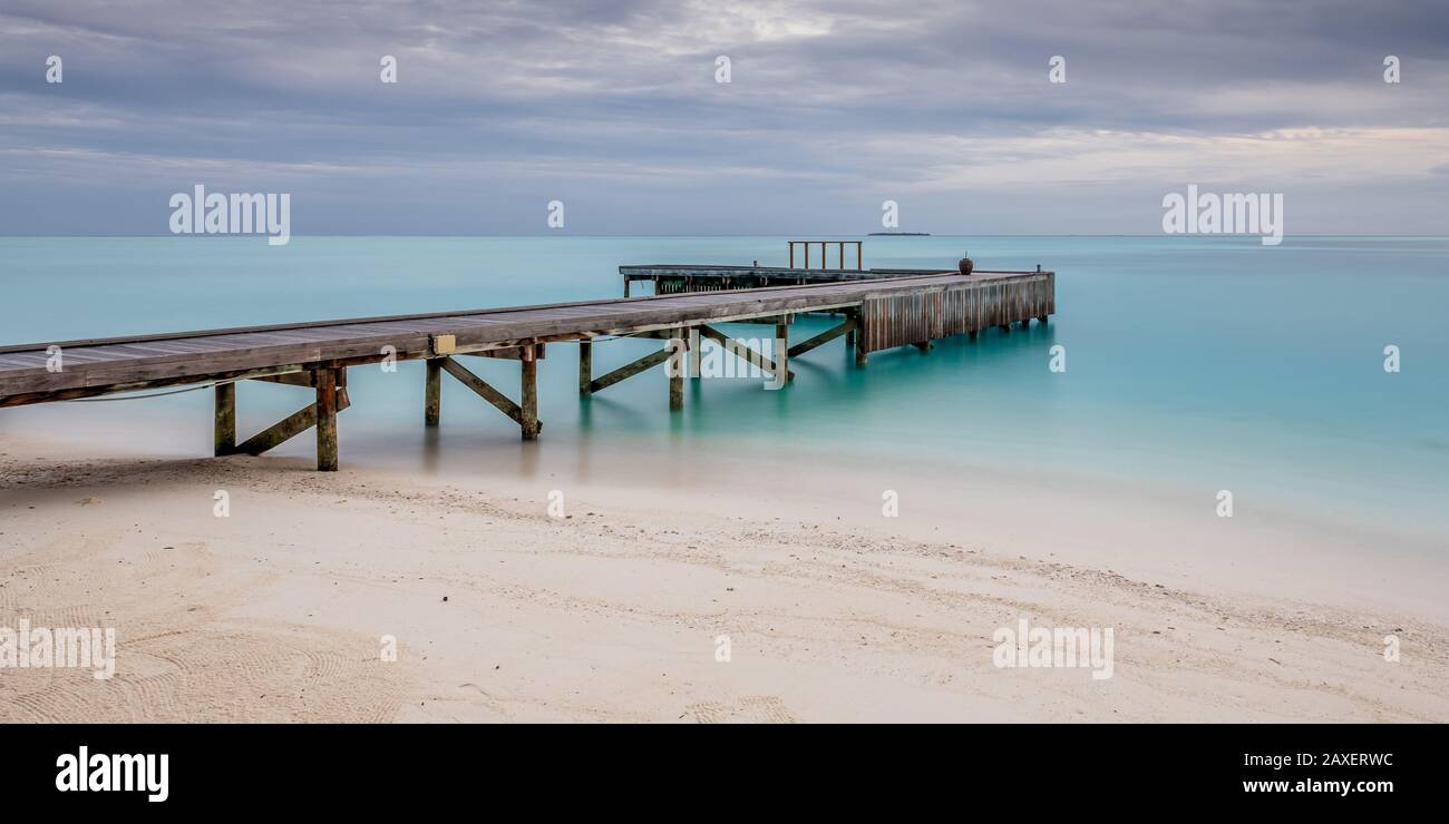 Ein langes Foto eines Piers, der von einem glattem türkisfarbenen Meer auf einer Insel auf den Malediven umgeben ist Stockfoto