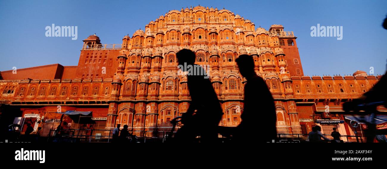Silhouette zweier Menschen, die vor einem Gebäude radeln, Hawa Mahal, Jaipur, Rajasthan, Indien Stockfoto