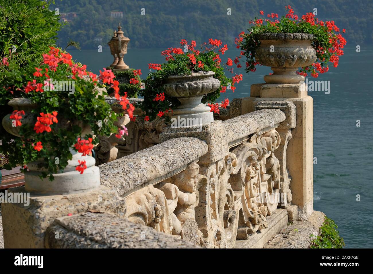 Villa del Balbianello Rotes Geranium in Urnen an einer verzierten Terrassenwand, Cherubs, Akanthuswirbel, Blick auf den Comer See, Lombardei Italien, Stockfoto