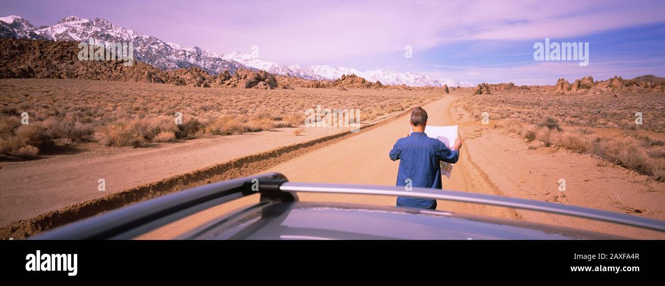 Rückansicht eines Mannes, der auf einer Feldstraße steht und einen Straßenkarte betrachtet, Kalifornien, USA Stockfoto