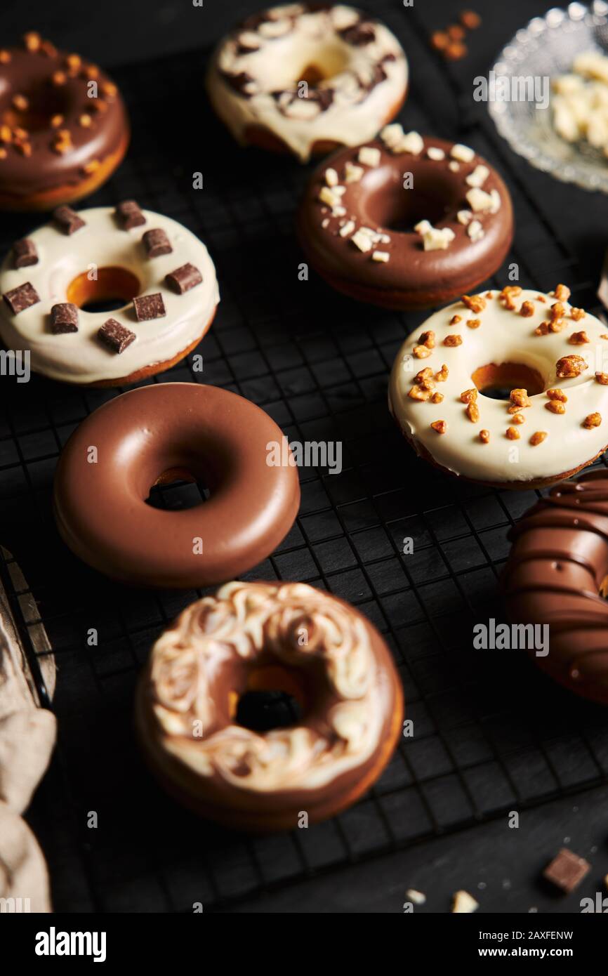 Vertikale Aufnahme von köstlichen Donuts in der weißen und bedeckt Braune Schokoladenglasur auf einem schwarzen Tisch Stockfoto