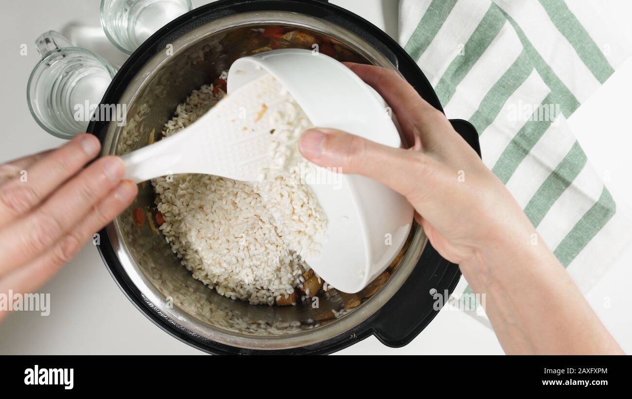 Das Kochen von Reis mit Fleisch und Gemüse im Druck Multi-Herd Schritt für Schritt, Draufsicht. Gießen von Reis in einen Topf. Stockfoto