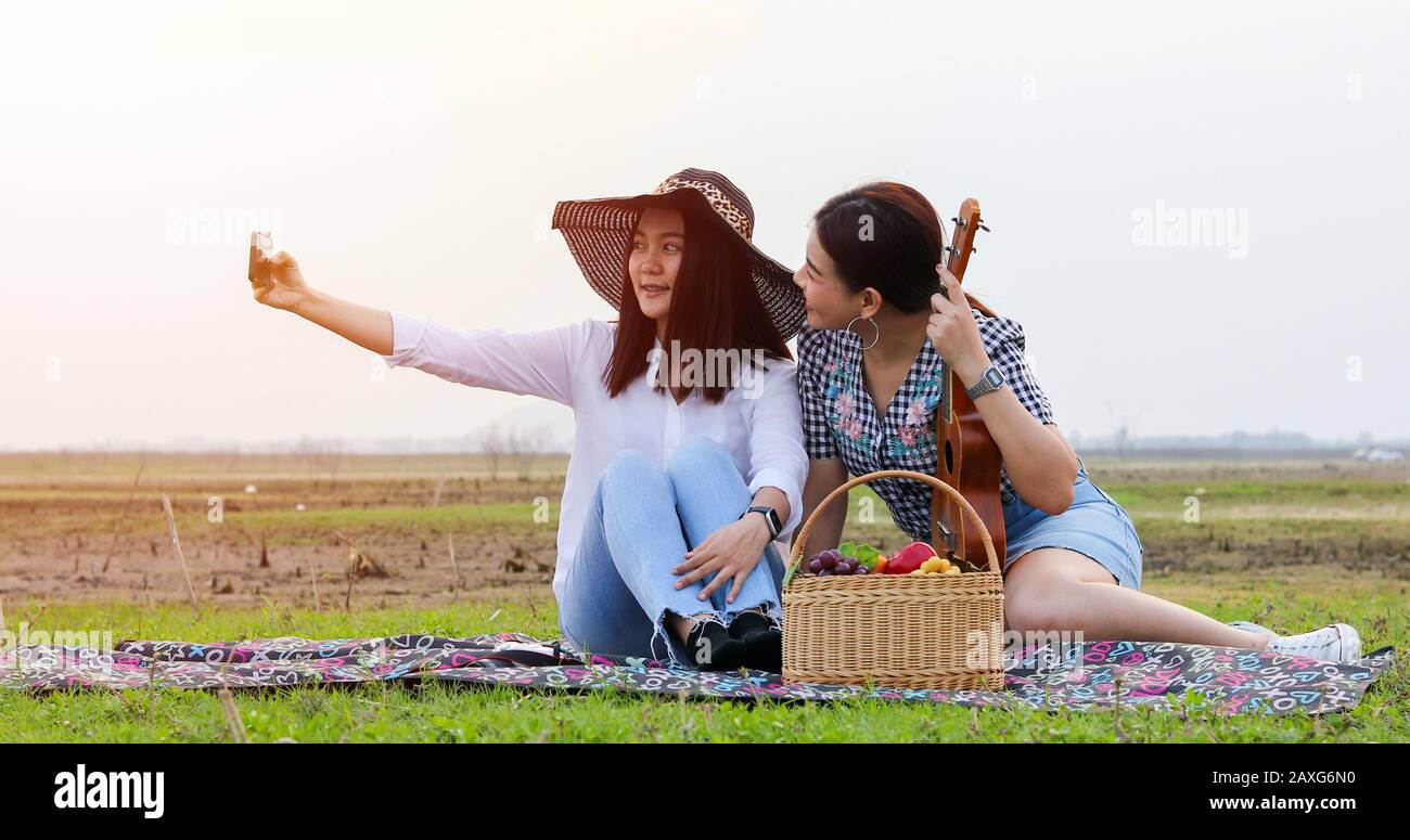 Eine Gruppe asiatischer Freunde, die Ukelele spielen und in den Sommerferien Zeit für ein Picknick verbringen.Sie sind glücklich und selfie, Entspannungszeit auf der Ferienkcon Stockfoto