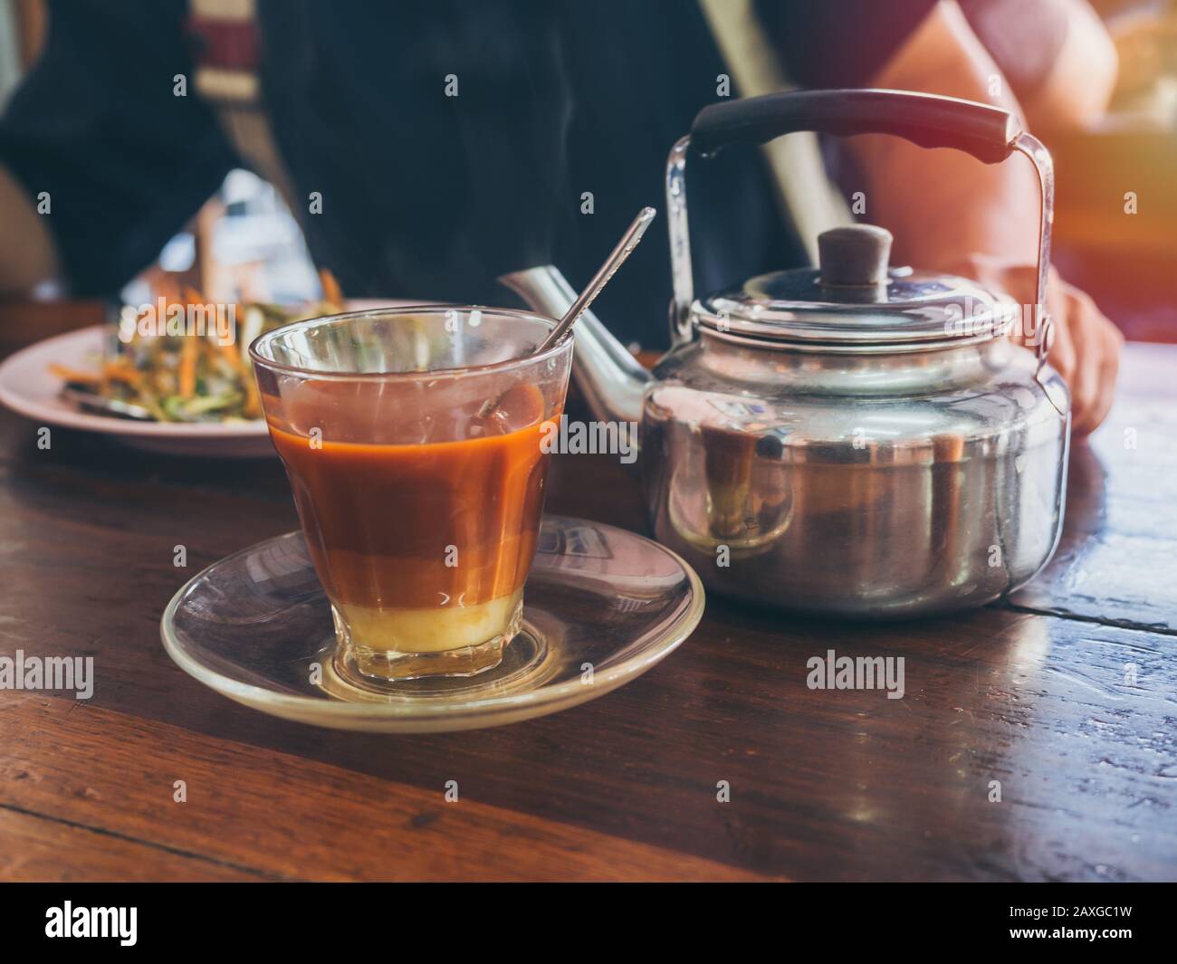 Frühstück im thailändischen Südstil, heißer thailändischer Tee aus Glas und ein alter Wasserkocher am Morgen auf Holztisch. Stockfoto