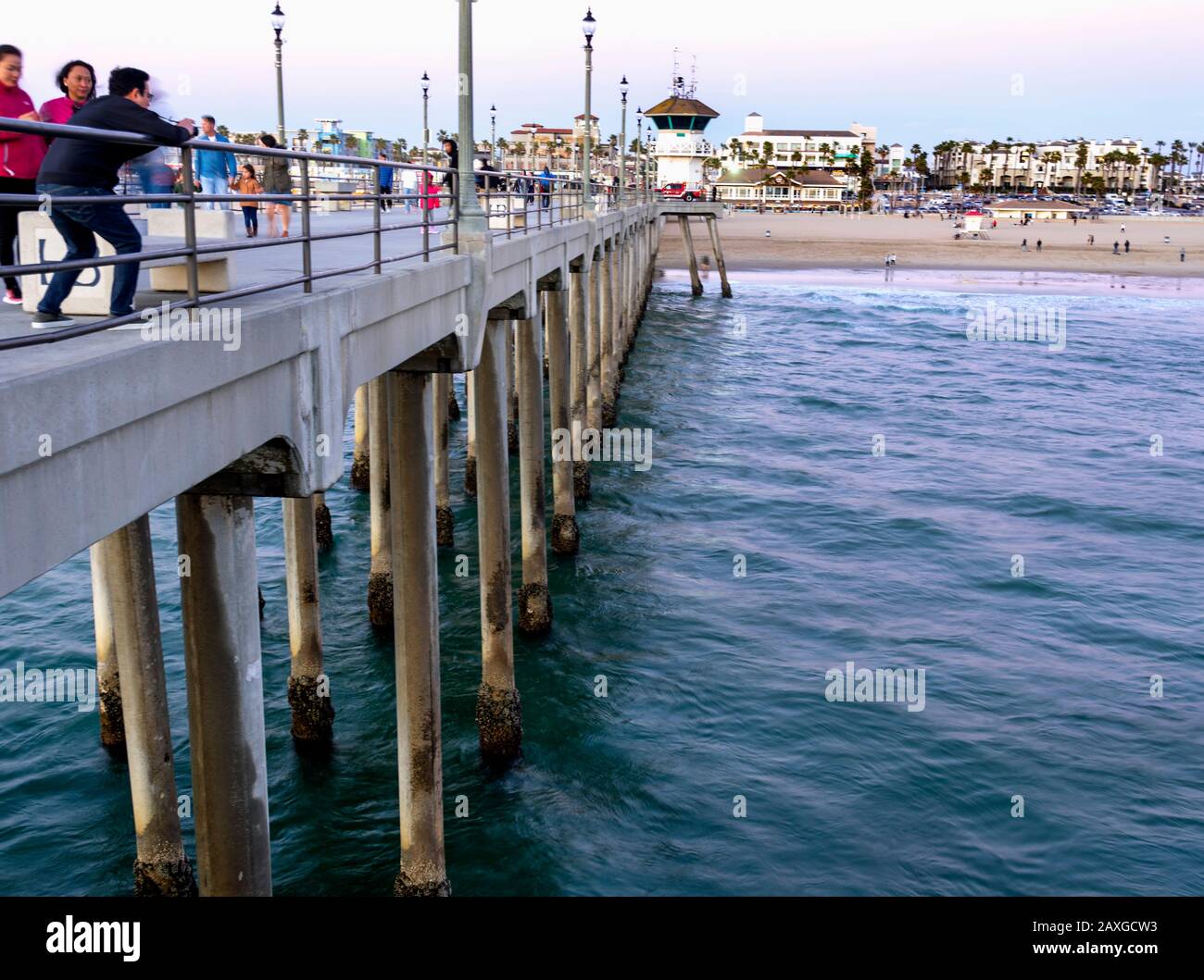 Viele Touristen, die während des Sonnenuntergangs auf dem Huntington Beach Pier spazieren, mit Blick auf die Stadt und den Strand. Stockfoto