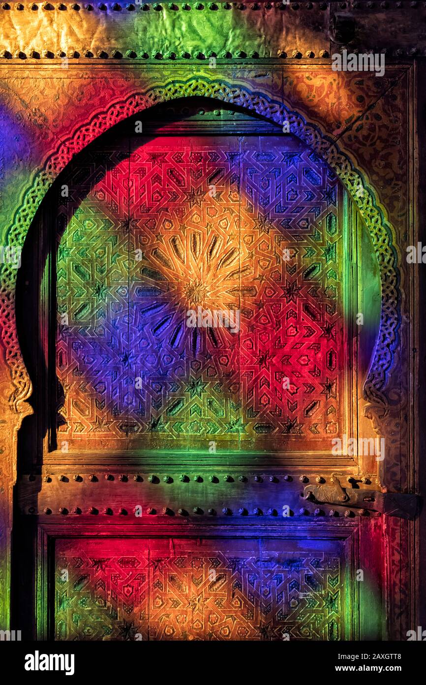 Traditionelle, alte, marokkanische Tür mit Holzschnitzereien, mit bunten Spiegelungen aus farbigem Glasfenster im Bahia Palast in Marrakesch, Marokko. Stockfoto