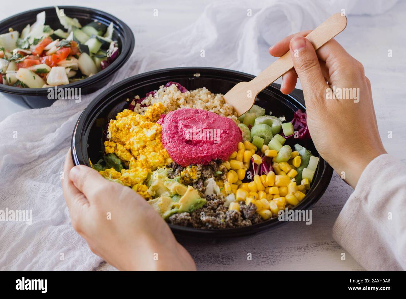 Buddha-Schüssel-Konzept für gesundes Essen. Veganer Detox-Salat mit Quinoa und Rübenhummus auf weißem Hintergrund. Instagram-Stil mit den Händen, die essen Stockfoto