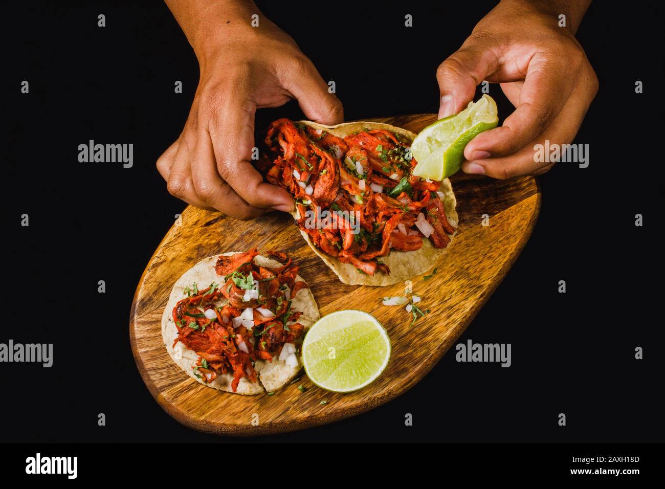 Tacos al Pastor-Wohnung lag auf einem schwarzen Hintergrund, auf dem eine Person Kalk drückte. Authentische mexikanische Tacos mit mariniertem Fleisch, Zwiebel und Ananas Stockfoto