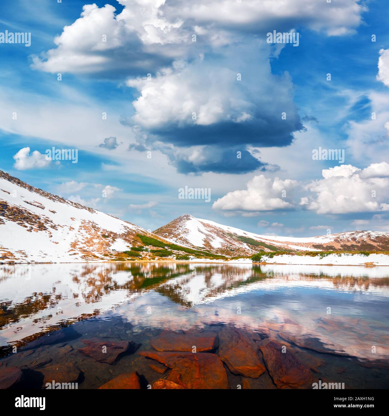 Wunderschöne Landschaft mit Bergsee und schneebedeckten Hügeln unter blauem bewölktem Himmel. Berge im Frühling. Landschaftsfotografie Stockfoto