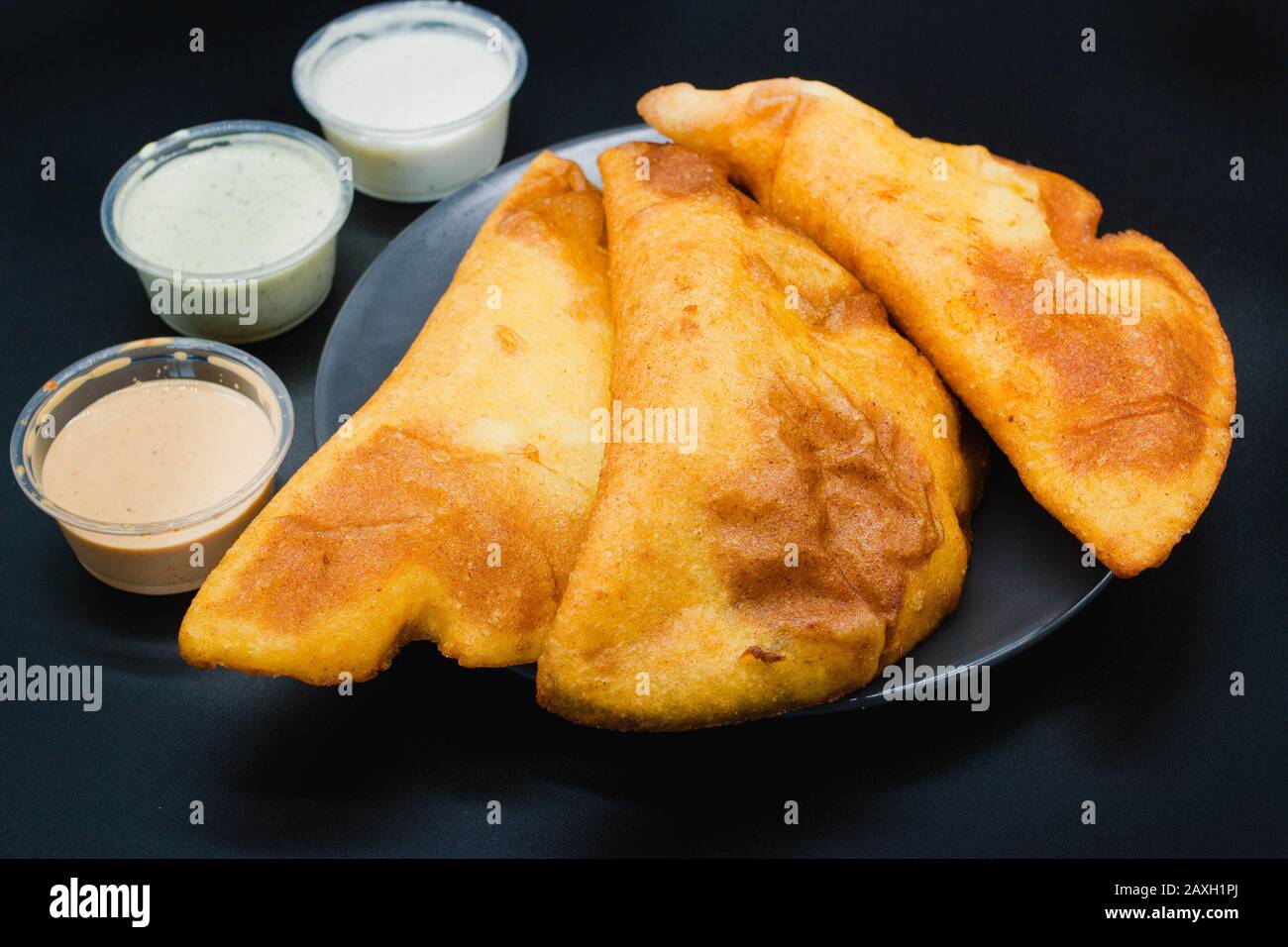 Empanadas venezolanas auf schwarzem Hintergrund mit verschiedenen Soßen wie Guasacaca und würziger Soße. Empanada aus Venezuela wird gebraten und mit Mais hergestellt Stockfoto