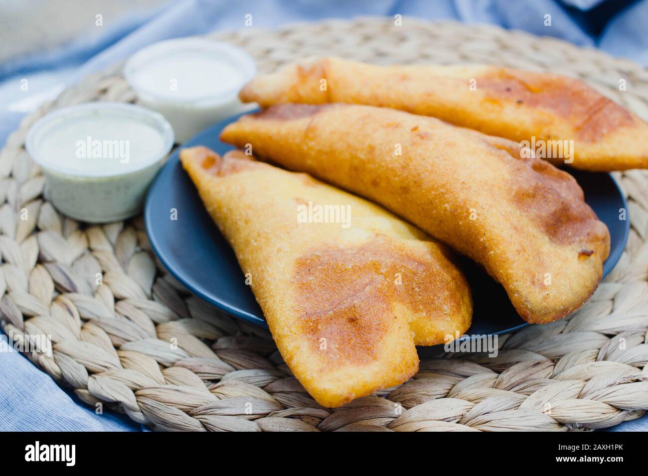 Empanadas venezolanas auf rustikalem Hintergrund mit verschiedenen Soßen wie Guasacaca und würziger Soße. Stockfoto