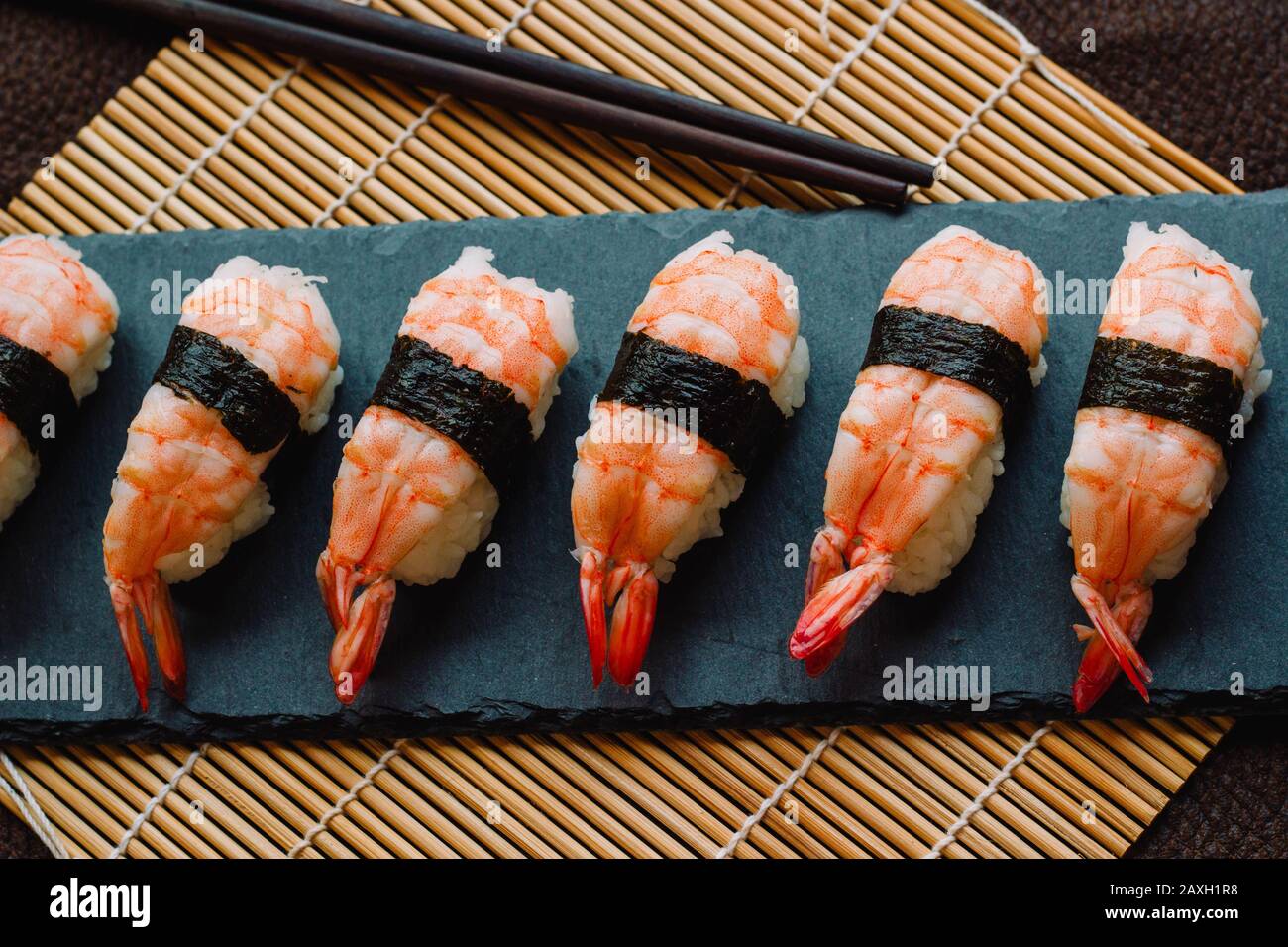 Nigiri sushi bereit, auf einem Schiefer mit Essstäbchen und einer traditionellen Bambusrollmatte zu essen Stockfoto