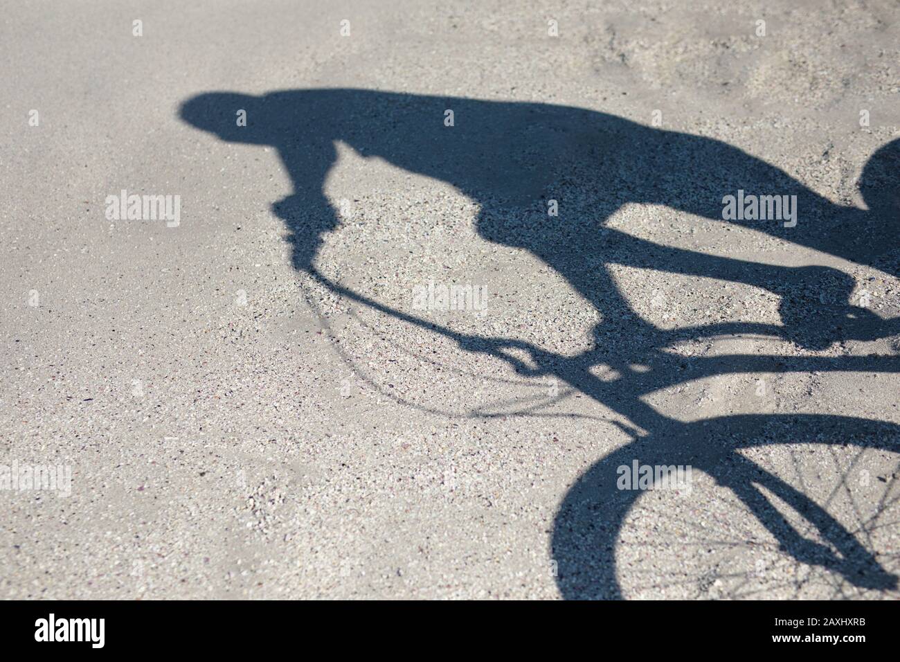 Seitenansicht des Schattens eines älteren afroamerikanischen Mannes, der an einem sonnigen Tag mit dem Fahrrad am Strand unterwegs ist Stockfoto