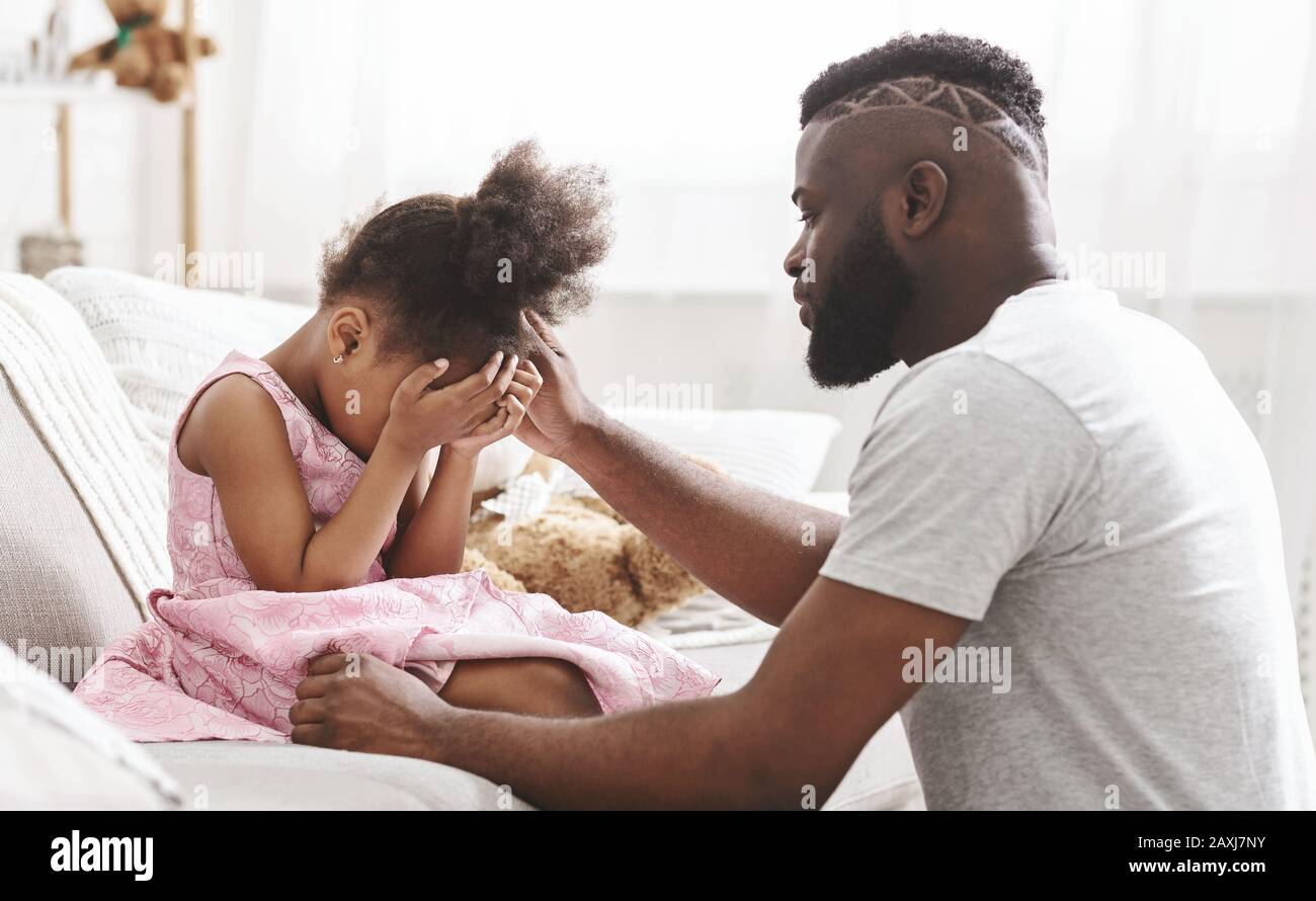 Afrikanischer Vater tröstet kleines weinendes Mädchen zu Hause Stockfoto