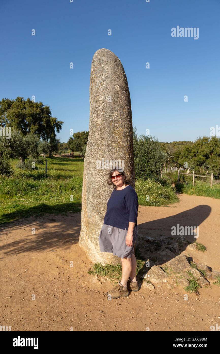 Frau mittleren Alters, die am jungsteinzeitlichen Stehstein 4 Meter hoch steht, heißt Menir dos Almendres, in der Nähe von Evora, Alentejo, Portugal Stockfoto