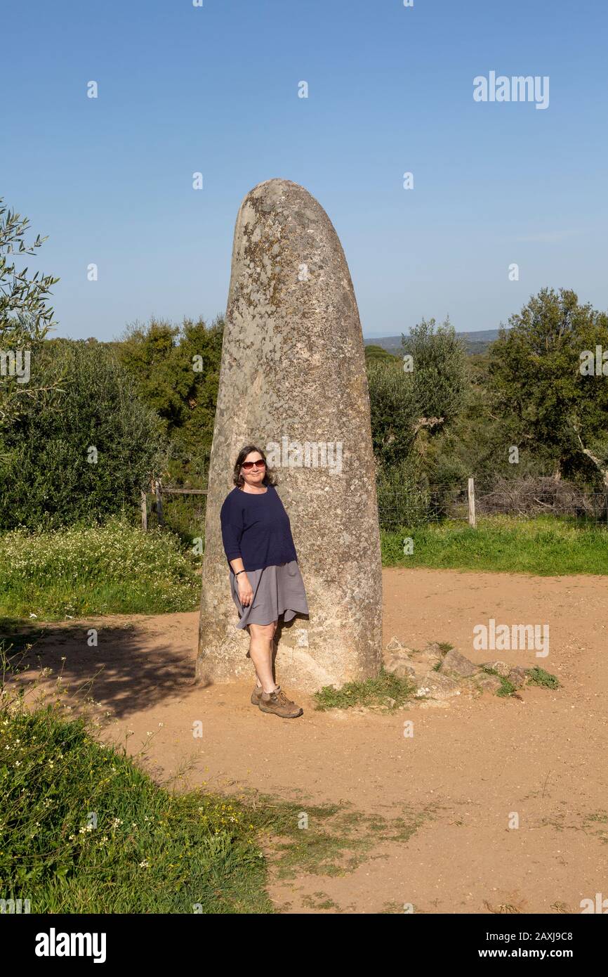Frau mittleren Alters, die am jungsteinzeitlichen Stehstein 4 Meter hoch steht, heißt Menir dos Almendres, in der Nähe von Evora, Alentejo, Portugal, Stockfoto