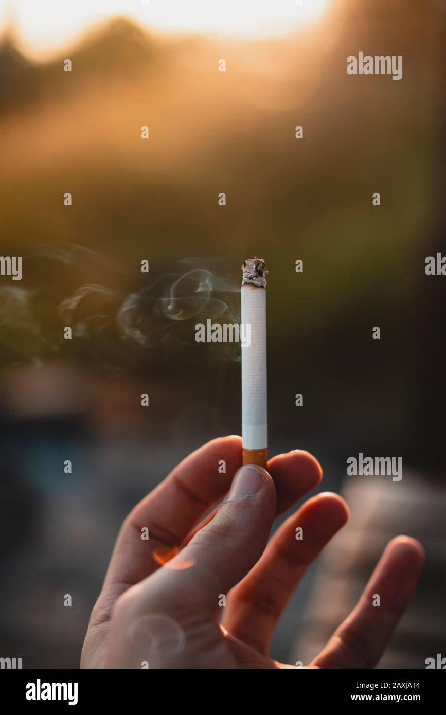 Person, die eine angezündete Zigarette in der Hand hält.Gesundheitseffekte des Zigarettenrauchens. Stockfoto