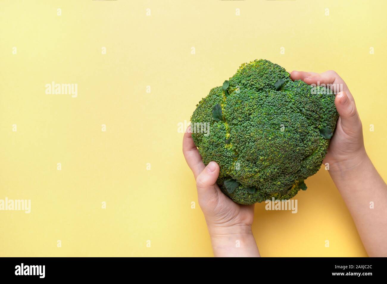 Brokkoli in Kinderhand auf gelbem Hintergrund. Draufsicht, Platz für Text. Stockfoto