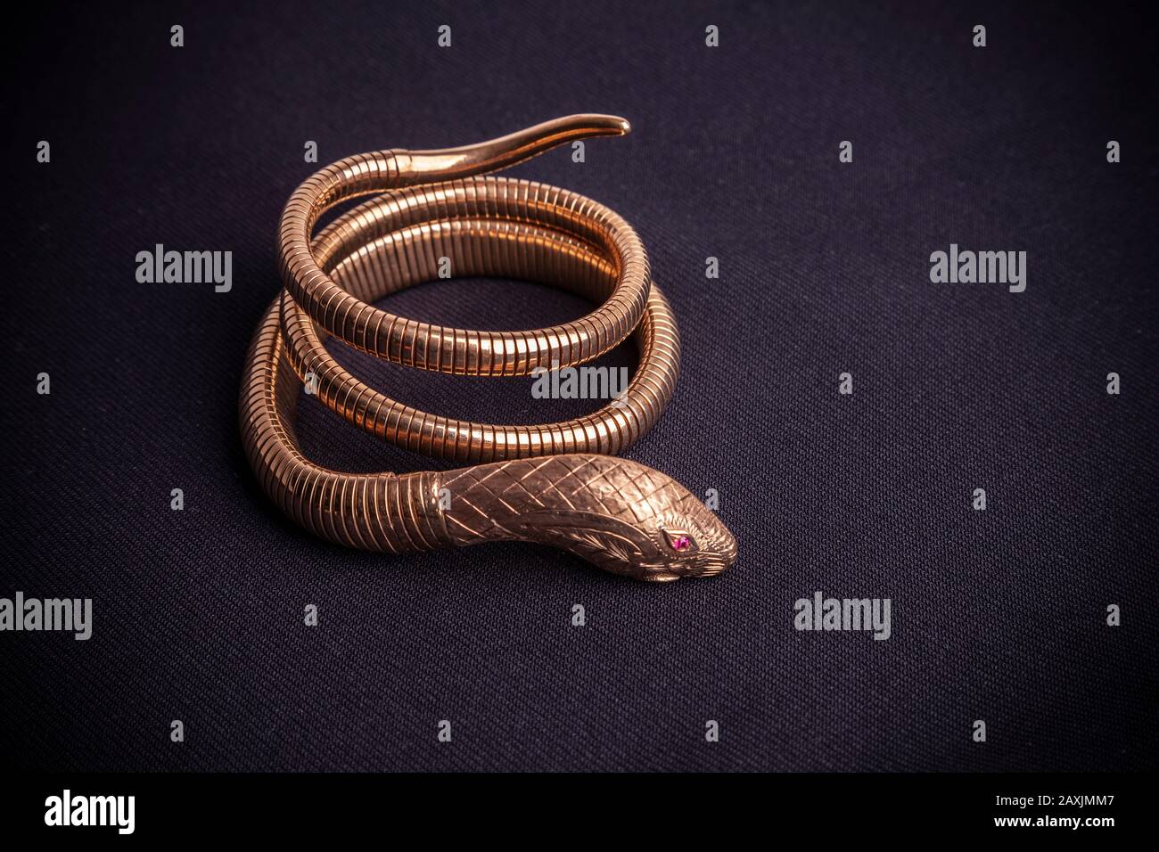 Armband im Stil des Gold Egyptian Revival, in Form einer Schlange mit Ruby-Augen auf schwarzem Hintergrund. Stockfoto