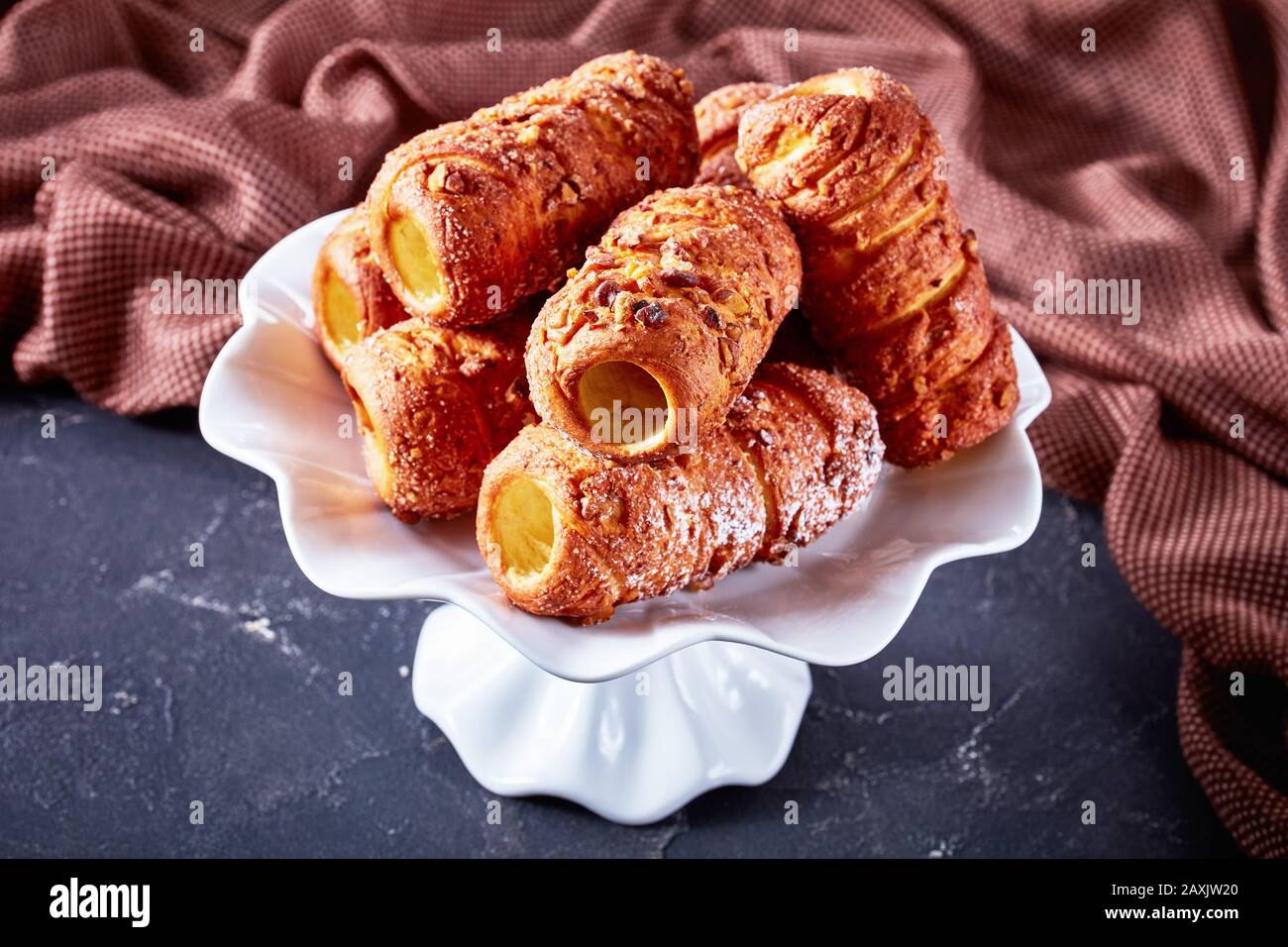 Europäisches traditionelles Dessert: Kaminkuchen oder Spitkuchen mit Zucker und Zimt, serviert auf einem weißen Kuchenständer auf dunklem Hintergrund, aus nächster Nähe Stockfoto