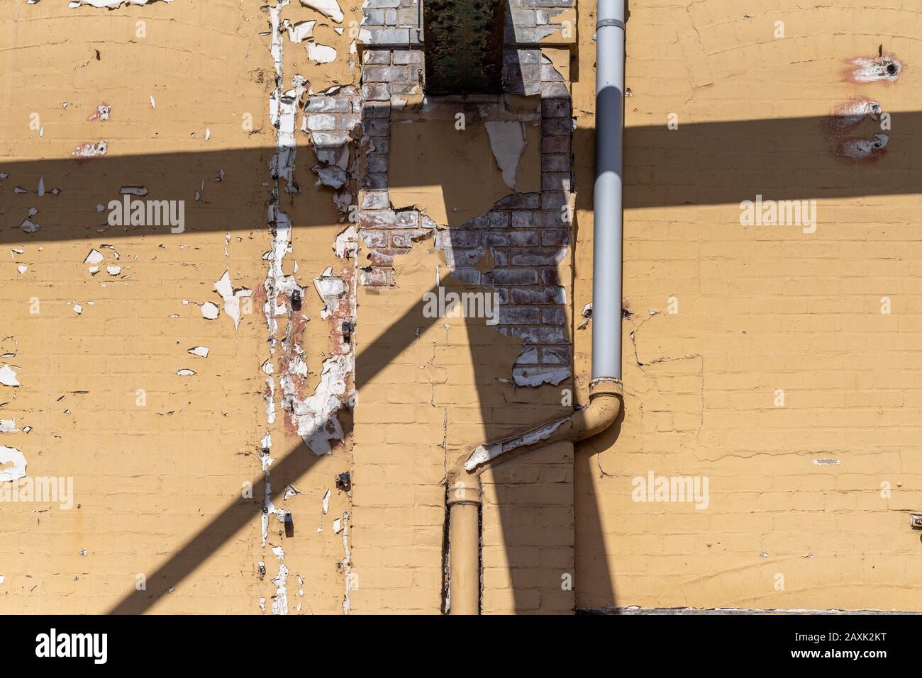 Schälende gelb lackierte, sonnenbeleuchtete Wand mit hartem Schatten und Drainpipe. Abstrakt in der Stadt. Stockfoto